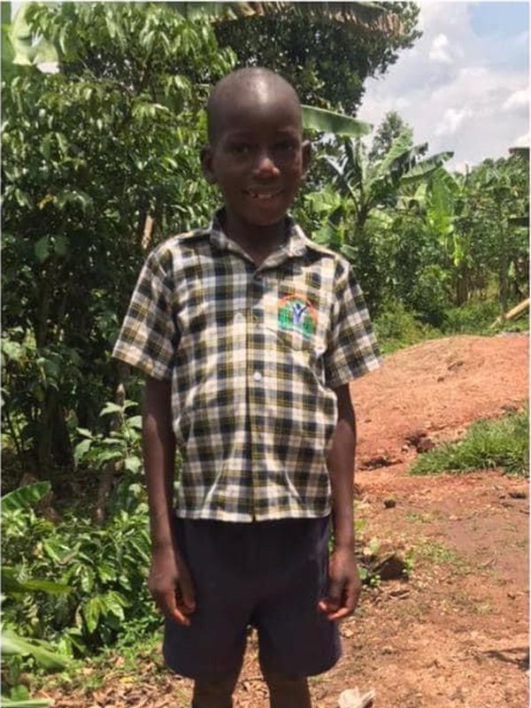 The same boy standing proudly in his school uniform, socks and shoes
