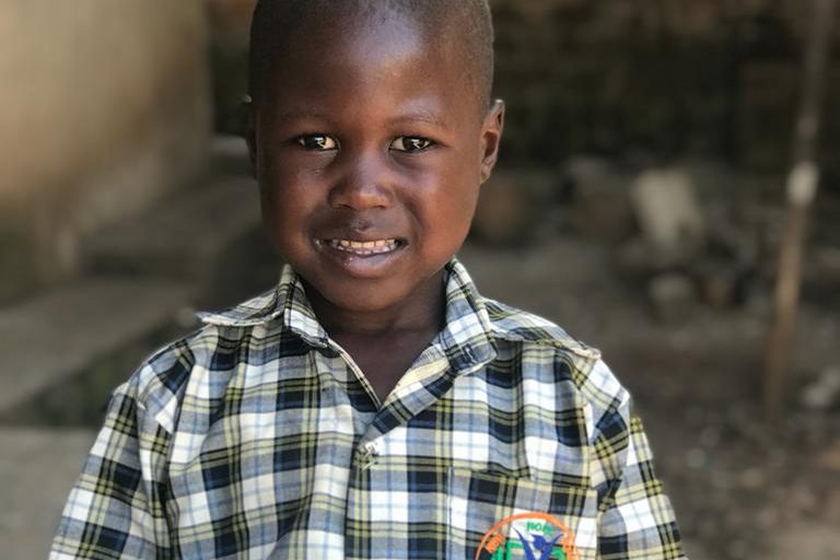 A smiling boy in his school uniform holding books and pencils