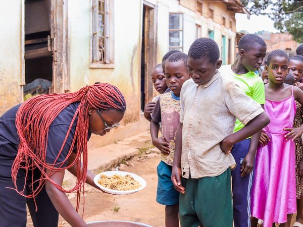 A volunteer serving a plate of food to waiting children