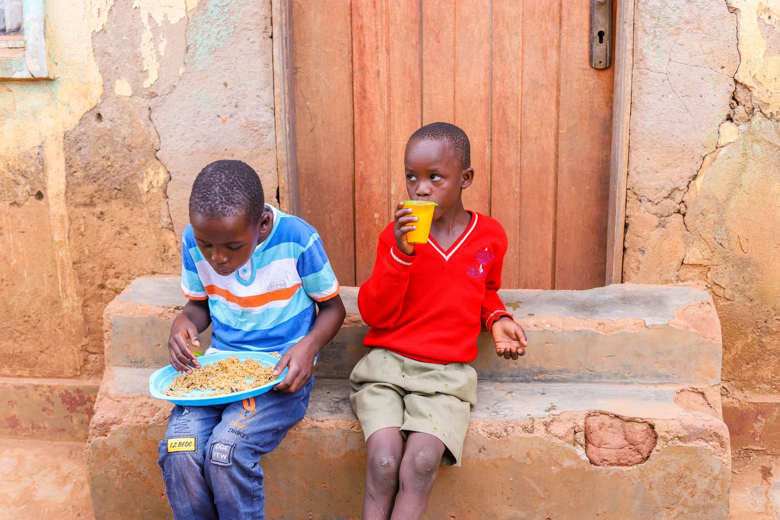 Two boys sharing a meal on a doorstep